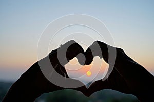 Heart shape formed with hands with the sun in the middle against blue sky