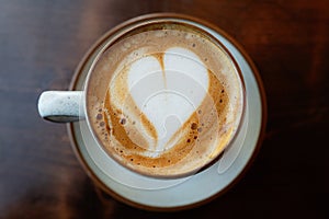 Heart shape in the froth of a flat white coffee in a cup and saucer on a dark wood table, seen from above