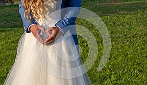 Heart shape with groom`s hands on the dress of the bride