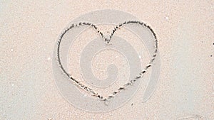 Heart shape handdrawing wiping and easing by ocean and sea wave on the white sand beach background. Passion and affection concept