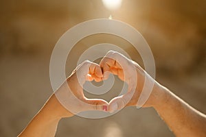 Heart shape by hands of the couple at the beach during sunrise, Portugal