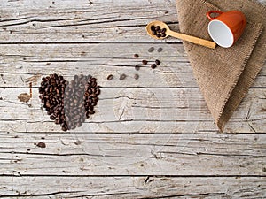 Heart shape made of coffee beans, wooden spoon and cup on wooden