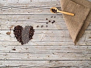 Heart shape made of coffee beans and wooden spoon on wooden back