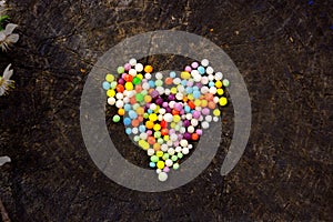 Heart shape made from colorful nonpareils sprinkle decorations. Wooden background.