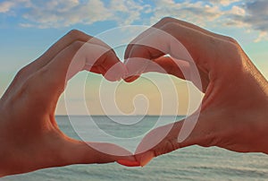 Heart shape made with hands of couple sunset background. Love symbol concept over seascape