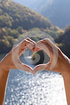 Heart shape, made by hands of women, on background of beautiful nature landscape. Love nature, travel, earth day concept
