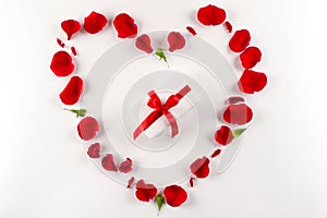 Heart shape made of red rose petals and white gift box with red ribbon on white background. Top view, copy space