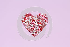 Heart shape made of a small heart shaped candy on pink background.