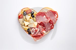 Heart shape made of traditional Spanish tapas, ham, salami, cheese and olives with bread. Flat lay with assorted appetizers for