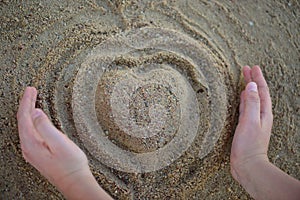 Heart shape making by hands from the sand on the beach. Top view.