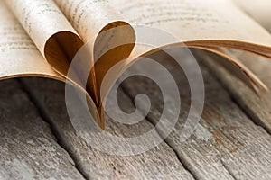 Heart shape from opened book pages on wood background.