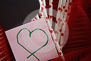 Heart shape ornamental straws and sticky note with a red background.