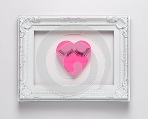 Heart shape pink paper with eyelashes  in frame on white background. Valentines or woman`s day background design. Minimal flat la