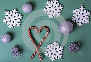 Heart shape with red Christmas candy canes, white large snowflakes, silvery balls on a green background, top view