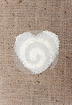 Heart shape rice grains on old sack background.