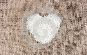 Heart shape rice grains on old sack background.