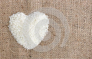 Heart shape rice grains on old sack background.