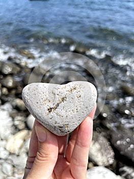 Heart shape stone in girls hand against background of beach. Summer sunny day. Love, wedding and Valentine day concept