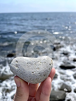 Heart shape stone in girls hand against background of beach. Summer sunny day. Love, wedding and Valentine day concept