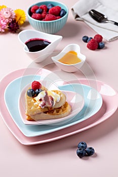 Heart shaped  belgian waffles with Ice-cream and berries on pink background. Tasty breakfast. Close-up