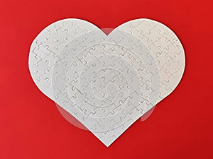 Heart shaped blank white jigsaw puzzle on red background puzzle pieces completing the heart shape