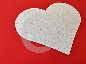 Heart shaped blank white jigsaw puzzle on red background puzzle pieces completing the heart shape