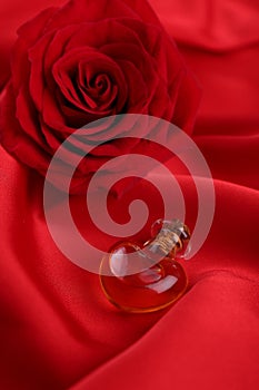 Heart shaped bottle of love potion and rose flower on red fabric