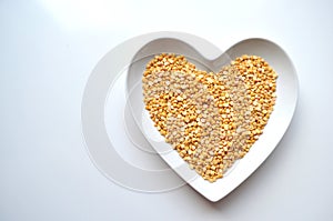 Heart shaped bowl of dry split yellow peas on white with copy space