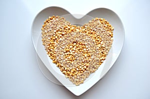 Heart shaped bowl of dry split yellow peas on white with copy space