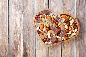Heart shaped bowl with mixed nuts on wooden table top view. Healthy food and snack