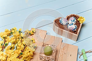 Heart shaped box with decorated Easter eggs, yellow flowers, burning candle on wooden blue background. Spring and Easter concept.
