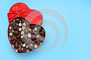 Heart shaped box with delicious chocolate candies on light blue background, top view. Space for text