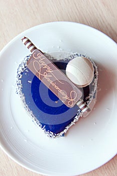 The heart-shaped cake is decorated with blue icing, almond macaroni and coconut topping with a chocolate happy anniversary