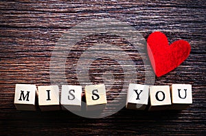 Heart shaped chewing candies and words miss you on cubes, wooden background. Free space for your text.