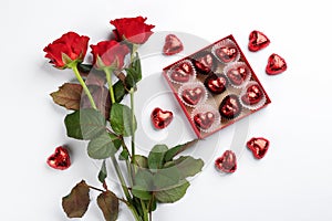 Heart shaped chocolate candies and bouquet on white background, top view