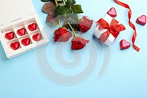 Heart shaped chocolate candies, gift box and bouquet on light blue background, flat lay. Space for text