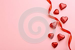 Heart shaped chocolate candies and ribbon on pink background, flat lay. Space for text