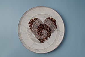 Heart shaped coffee beans, on a white marble plate. Top view