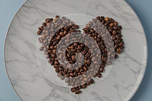 Heart shaped coffee beans, on a white marble plate. Top view