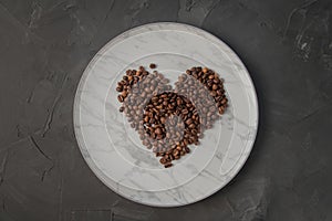 Heart shaped coffee beans, on a white marble plate. Top view