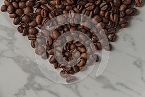 Heart shaped coffee beans, on a white marble plate. Top view