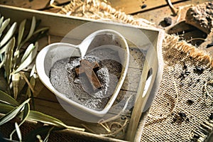 Heart-shaped container with ashes and wooden cross on wooden tray