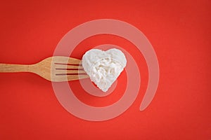 Heart shaped cooked rice with a fork on red background.