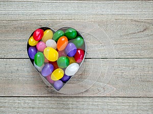 Heart shaped cookie cutter with jelly beans on wood background