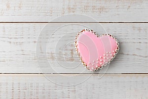 Heart shaped cookie decorated by pink glaze on a wooden white background with copy space