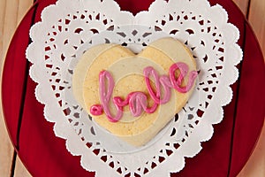 Heart shaped cookie iced with pink cream in text babe on wooden table