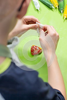 Heart-shaped cookie lies on a green coffee table. The child`s hands squeeze the white icing out of the tube creating decorations.
