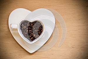 Heart shaped cup with coffee beans on wooden table