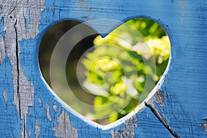 Heart-shaped cutout in an old blue wooden door overlooking a garden