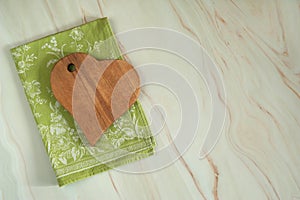 A heart-shaped cutting board made of beech wood and a beautiful green linen napkin on a pastel green marble background.